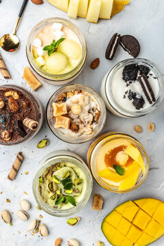 collection of delicious ice cream served in a glass jar, italian dessert gelato pistachio, chocolate, caramel, melon, mango, chocolate chip sandwich cookies, vertical image. top view