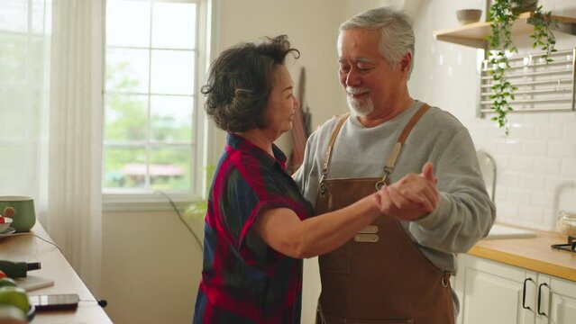 Asian senior couple enjoy romantic Cropped shot of a senior couple dancing during cooking healthy food together in kitchen at home.lifestyle of elderly couple after retirement and insurance concept