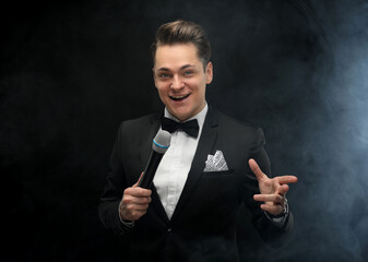 Stylish young man in a tuxedo holding a microphone, posing against a dark background with smoke