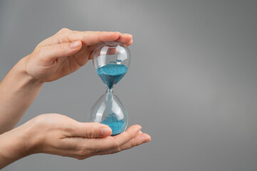 Woman holding an hourglass on a gray background. Close-up. Copy space. 