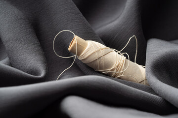 A reel with white threads in a draped soft gray fabric, close-up, macro. Atelier, tailoring, sewing...