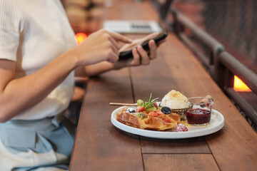 Woman using smartphone and eating dessert with fresh berries and fruit at cafe