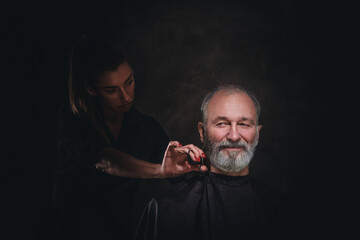 Studio shot of professional woman barber with scissor and her elderly customer.