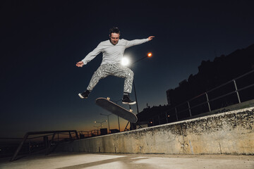 Portrait of professional skateboarder dressed in white casual clothes jumping skateboard.