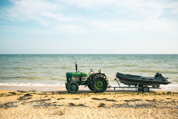 An old tractor towing a boat on the beach