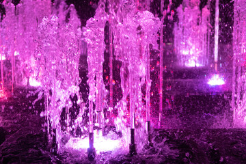Colorful water in the singing fountain. Colored light splashes closeup during the beautiful fountain show at night.