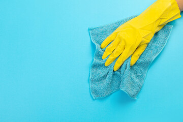 worker hand in a yellow rubber protective glove with micro fiber blue cloth wiping a blue wall from dust. A maid or housewife takes care of the house. Commercial concept for a cleaning company.