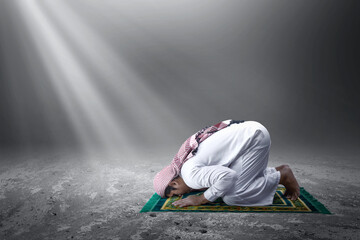 Muslim man with keffiyeh with agal in praying position (salat) on the prayer rug
