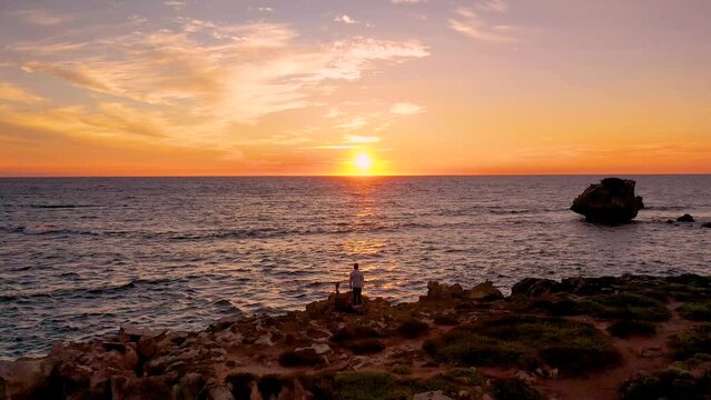 A man is standing, looking at beautiful sunset, beach, and sky in Point peron, Western Australia