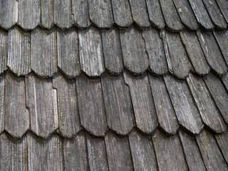 Old wood shingle roof with rough surface, background. Wooden planks on the top of a building. Weathered tiles on the roof. The texture of dark wood in the form of wooden tiles.