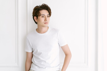 Attractive fashionable Asian man with earring, casual white t-shirt and standing over white...