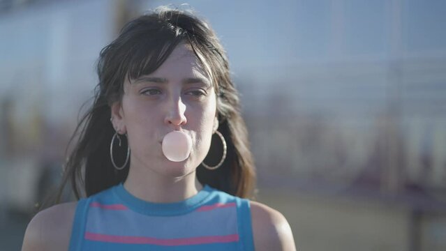 Close frontal view of dark-haired girl blowing bubble with chewing gum