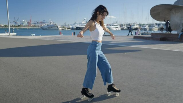 Lone girl in jeans and white top roller skates by harbor in sunlight