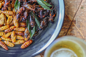 Crispy insects are served in black ceramic plates placed on tables made of steel grates, and fried...