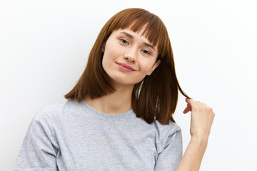 a sweet, shy, beautiful, red-haired woman in a gray T-shirt stands on a white background and looks sweetly into the camera while straightening her hair with her hand