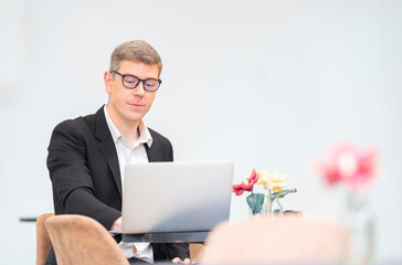 Lifestyle, Technology Concept - Businessman wearing formal black suit using laptop, thinking while relaxing in cafe during free time with copy space, entrepreneur working online.