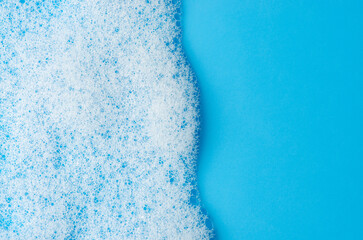 Texture of white foam on a blue background. Cleansing mousse for the face or bath foam or washing powder. Closeup. Copy space - obrazy, fototapety, plakaty