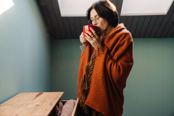 White mature woman wrapped blanket drinking tea