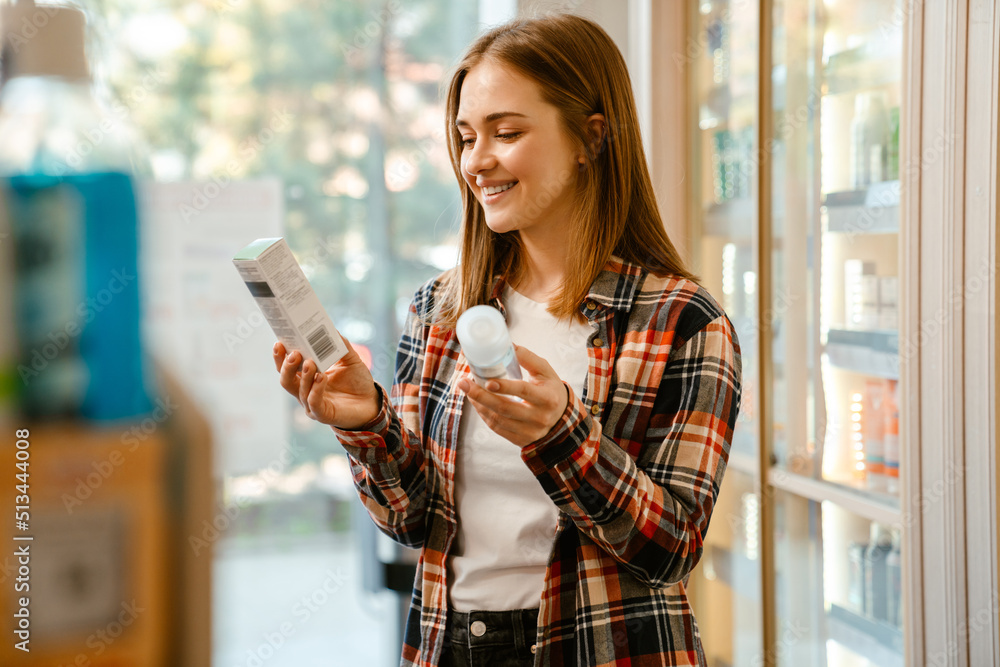 Wall mural young ginger woman smiling while choosing products in pharmacy