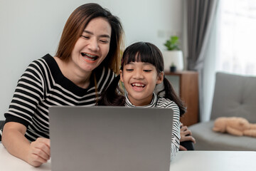 Fototapeta premium Asian little young girl kid learning online class at home with mother. Preschool child use laptop computer do homework, homeschool from school teacher by digital remote internet with support from mom.