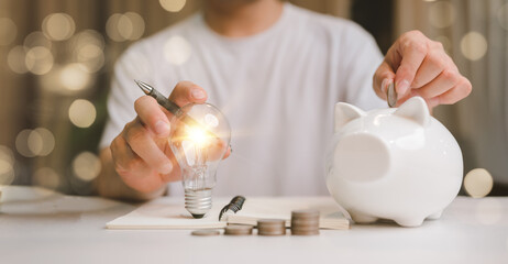 business man hand holding lightbulb and putting coin in to the piggy bank. idea saving energy and...
