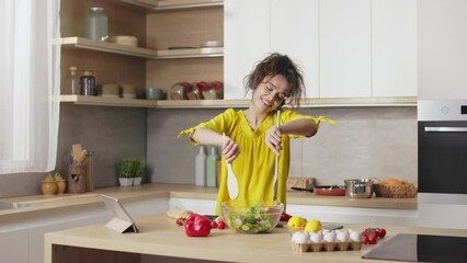 Joyful young woman with curly hair enjoying cooking process in wireless headphones with favorite music. Concept of people, happiness and domestic lifestyles.