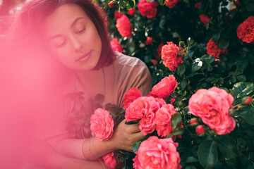 Young woman with pink hair enjoying flower fragrance in beautiful rose garden.
