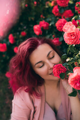 Young woman with pink hair enjoying flower fragrance in beautiful rose garden.
