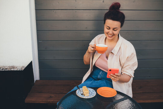 Young woman using smartphone while drinking cofee in a coffeehouse.