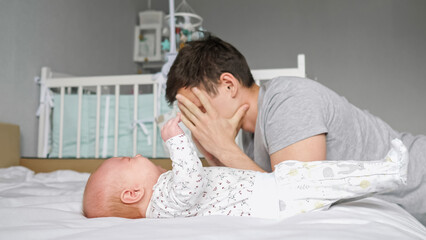 Tired father sits near loud newborn daughter lying on parent bed at home and waits baby girl calms...