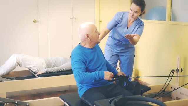 Professional female physiatrist controlling older man exercising with pilates ring to strengthen muscles. Physical medicine and rehabilitation concept