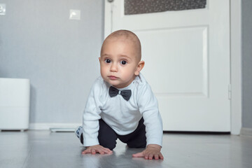Cute smiling baby boy crawls across room on call parents. Child in shirt with bow tie happily crawls to parents. Happy childhood concept