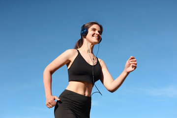 Young woman listening to music while running outdoors in morning, low angle view