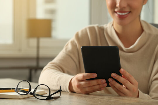 Young woman using e-book reader at wooden table indoors, closeup. Space for text