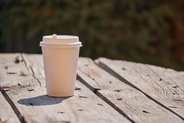 paper cup with coffee on a wooden table in the morning light