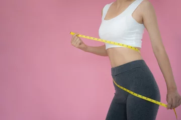 Poster Slim woman in sportswear measures her waist using tape measure on pink background. diet woman and lose weight plan © Shisu_ka