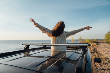 Young woman standing with arms outstretched through sun roof of car