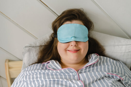 Smiling woman wearing sleeping eye mask resting on bed at home