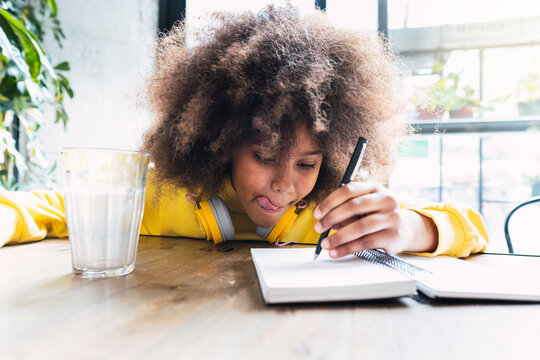 Girl with Afro hairstyle writing in notebook sitting in cafe