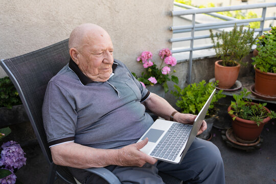 Senior man with laptop sitting on balcony