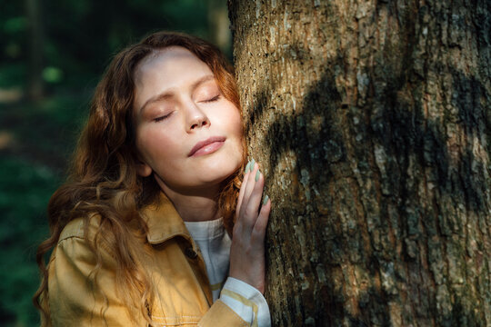 Woman with eyes closed embracing tree in forest