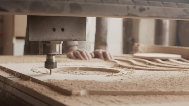 Woodworking CNC router carving circles out of wooden plank leaving sawdust everywhere in workshop