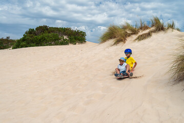 Children having fun while sliding down sand dune on sandboard, Kangaroo Island, South Australia - obrazy, fototapety, plakaty