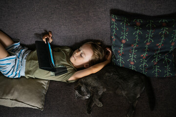 Boy lying on sofa using digital tablet computer playing games or watching cartoons at home. Child internet safety concept. Kid using electronic equipment. Parental control. Online education.