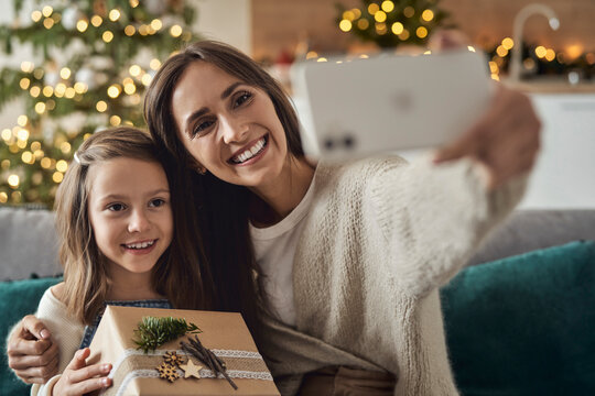 Smiling woman taking selfie with daughter through smart phone at home