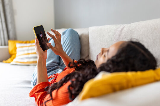 Young woman switching off smart phone lying on sofa at home