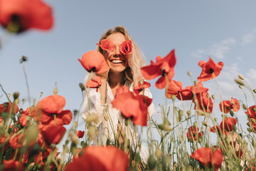 Happy woman covering eyes with flower in poppy field