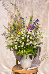 Fototapeta na wymiar Bouquet of wildflowers with chamomiles, cornflowers, foxglove, ivan tea, herbs in a white jug on a chair. Arrangement made by a florist.