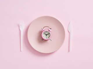 Alarm clock on pink plate with knife and fork. Intermittent fasting, lunchtime, weight loss, meal...
