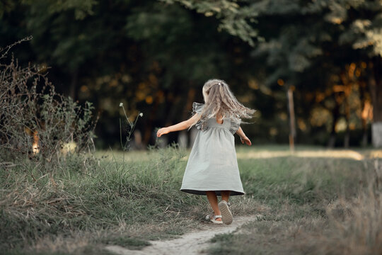 beautiful little girl with long hair plays, spins in a dress. Walk in the park, summer vacation, concept of family vacation, leisure and outdoor activities.